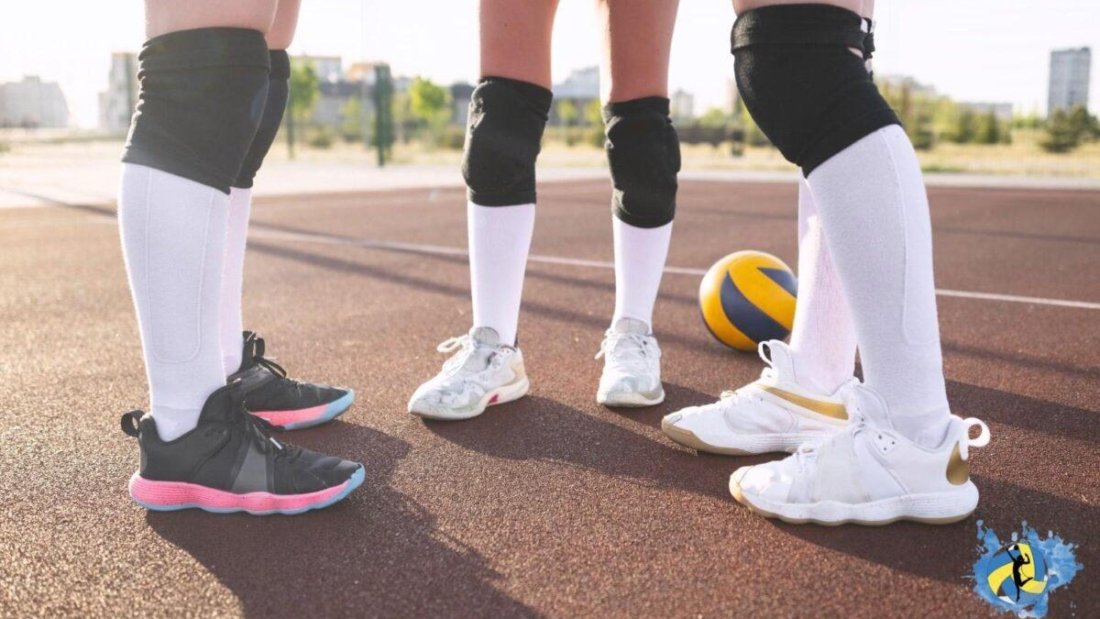 Three players standing in a outdoor court ahead of a yellow volleyball