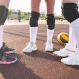 Three players standing in a outdoor court ahead of a yellow volleyball