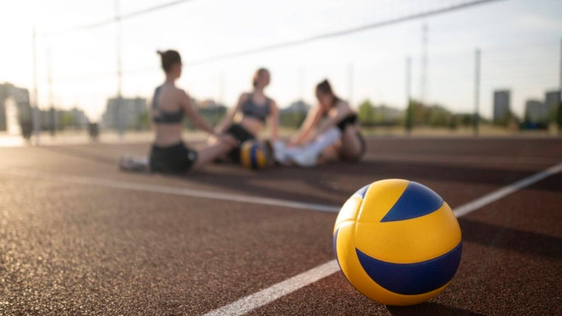 girls wearing volleyball gears in a volleyball court behind the volleyball