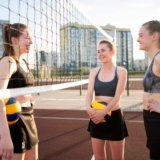 Three young female volleyball players discussing top volleyball shoes on an outdoor court.