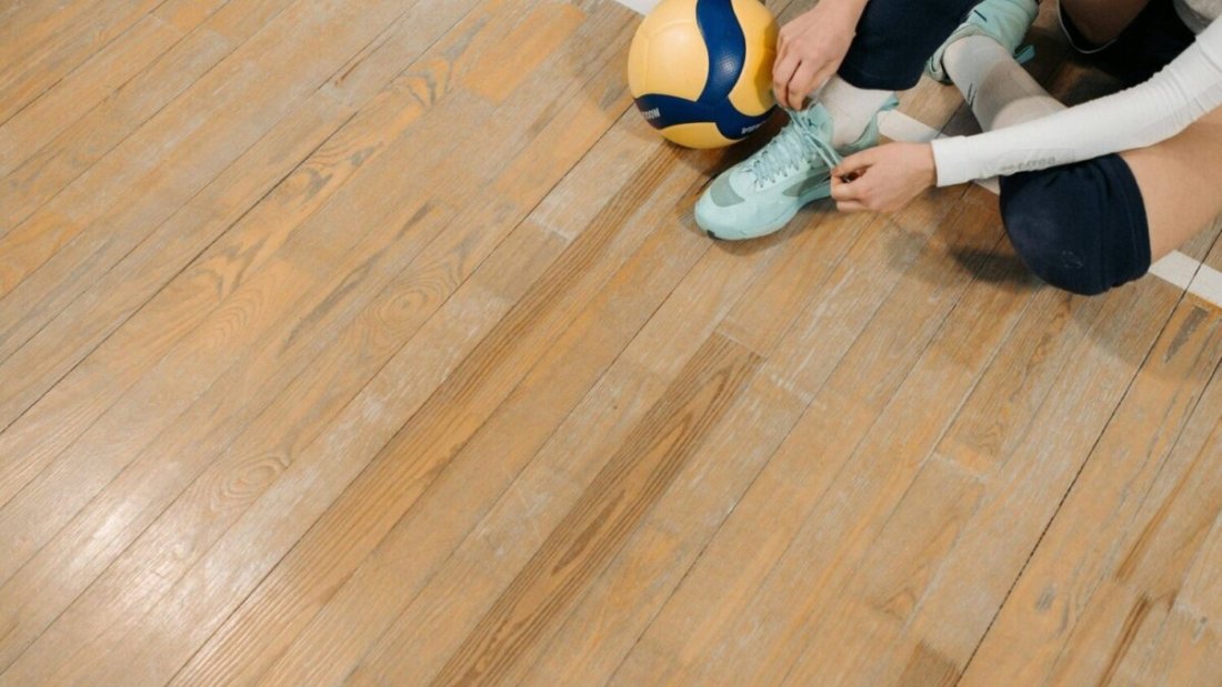 Girl tying the laces of cushioned volleyball shoes on an indoor court, with a volleyball beside her.