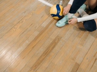 Girl tying the laces of cushioned volleyball shoes on an indoor court, with a volleyball beside her.