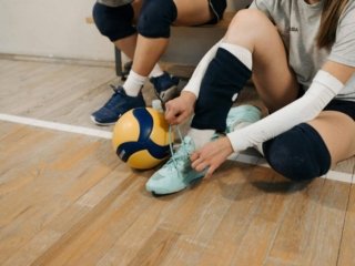 Girl tying her shoe laces with a volleyball by her side, sitting on a gym floor. with comfortable volleyball shoes