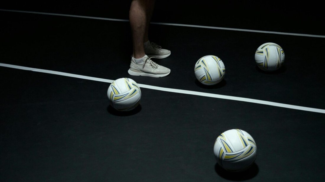 White Mizuno volleyball shoes and a white volleyball on a black court.