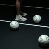 White Mizuno volleyball shoes and a white volleyball on a black court.