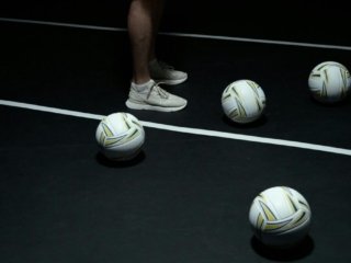 White Mizuno volleyball shoes and a white volleyball on a black court.