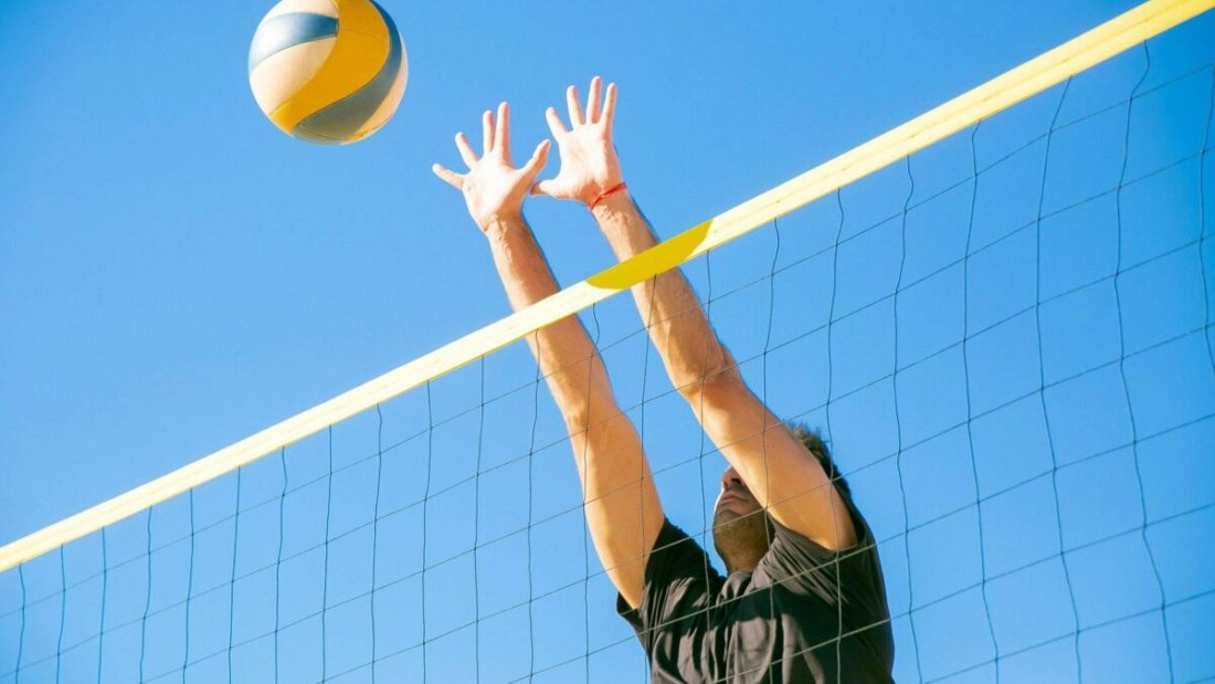 Man pushing a volleyball on an outdoor court, showcasing the durability of volleyball shoes designed for tough surfaces.