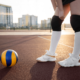 a girl in outdoor volleyball court with a volleyball in front of her wearing technology volleyball shoes