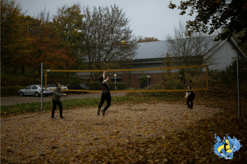 Three men's playing volleyball on outdoor court in rainy whether