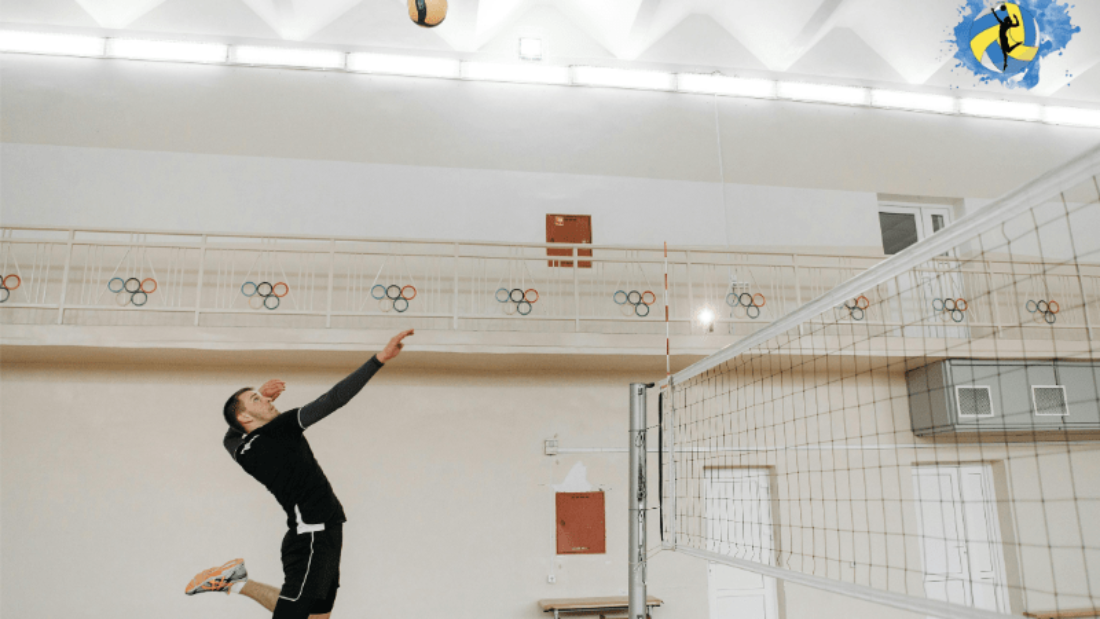 A male volleyball in air to hit a volleyball to other side in the indoor volleyball