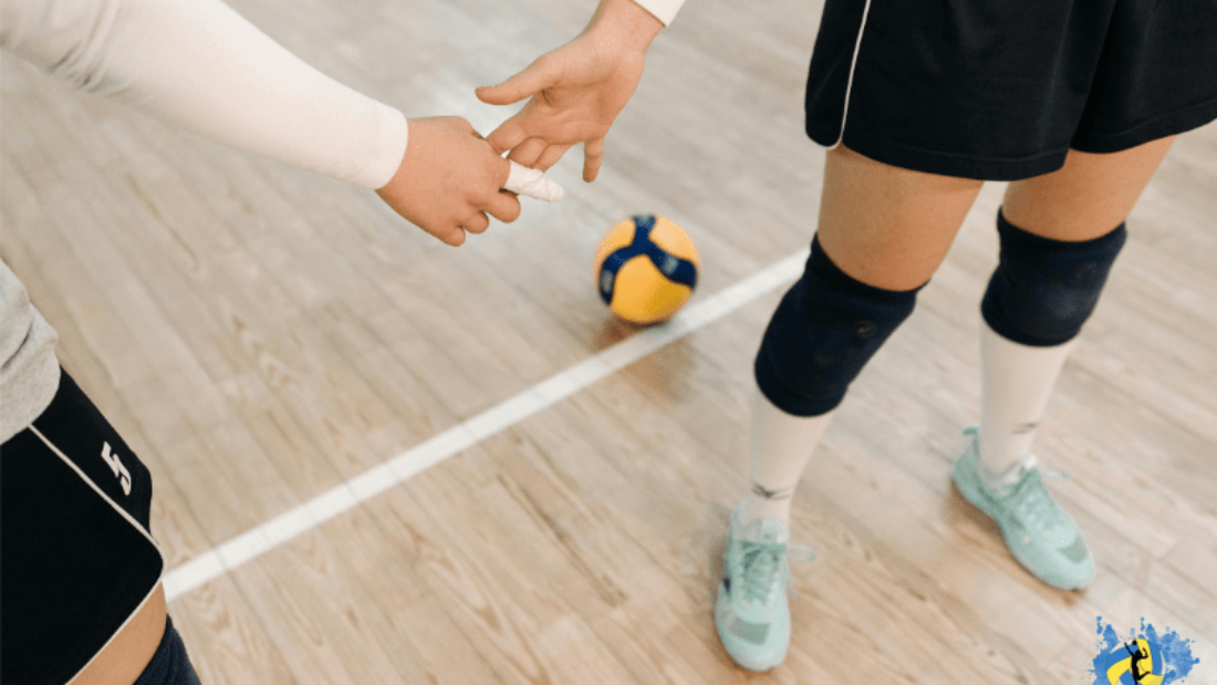 Two women holding hands in indoor volleyball court with a volleyball in background